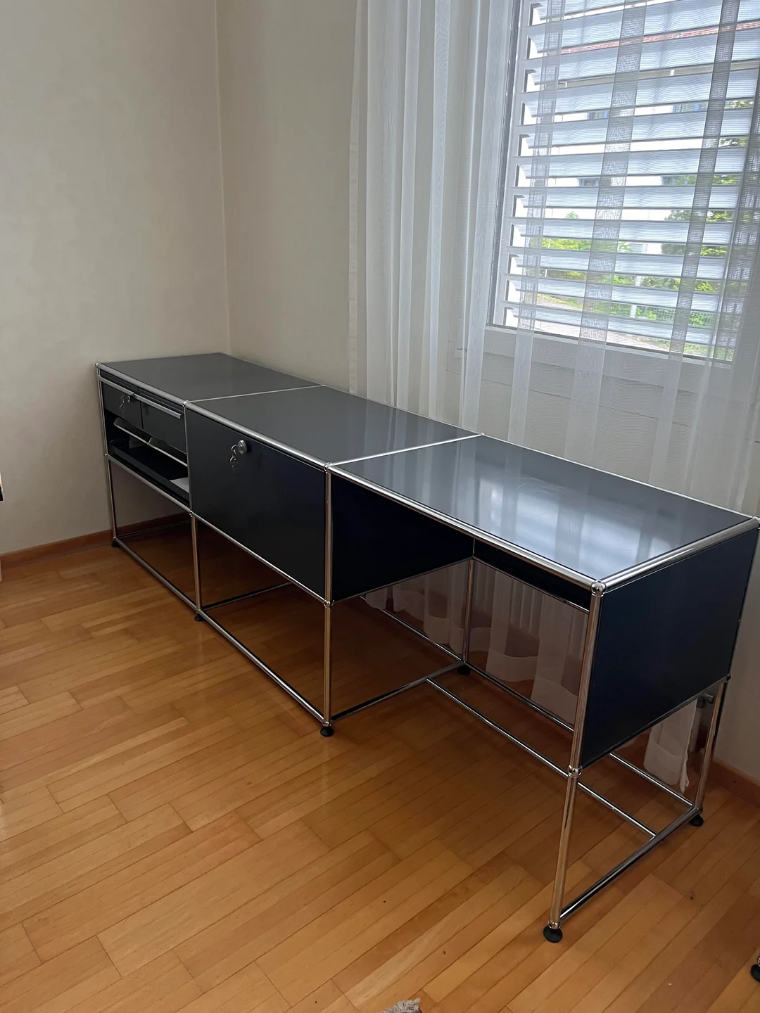 Dark modular steel desk under a window in a home office with wooden floors