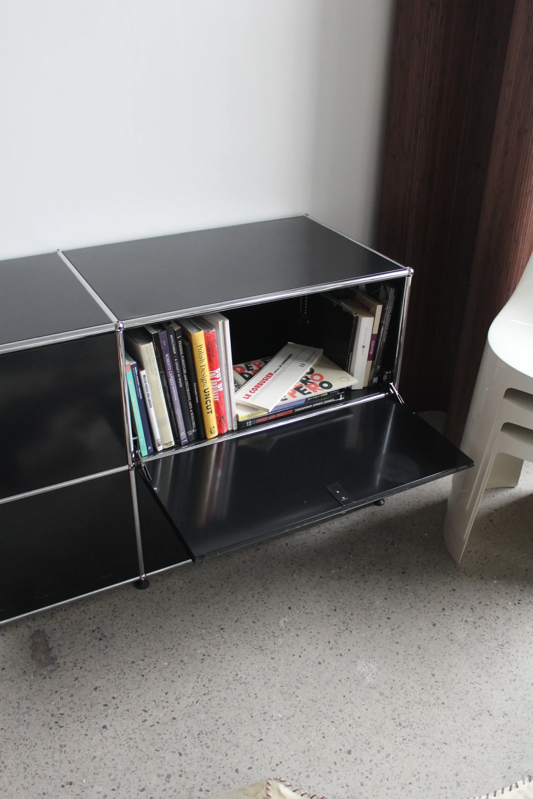 Black modular steel storage unit with an open compartment holding a row of books and magazines next to closed compartments