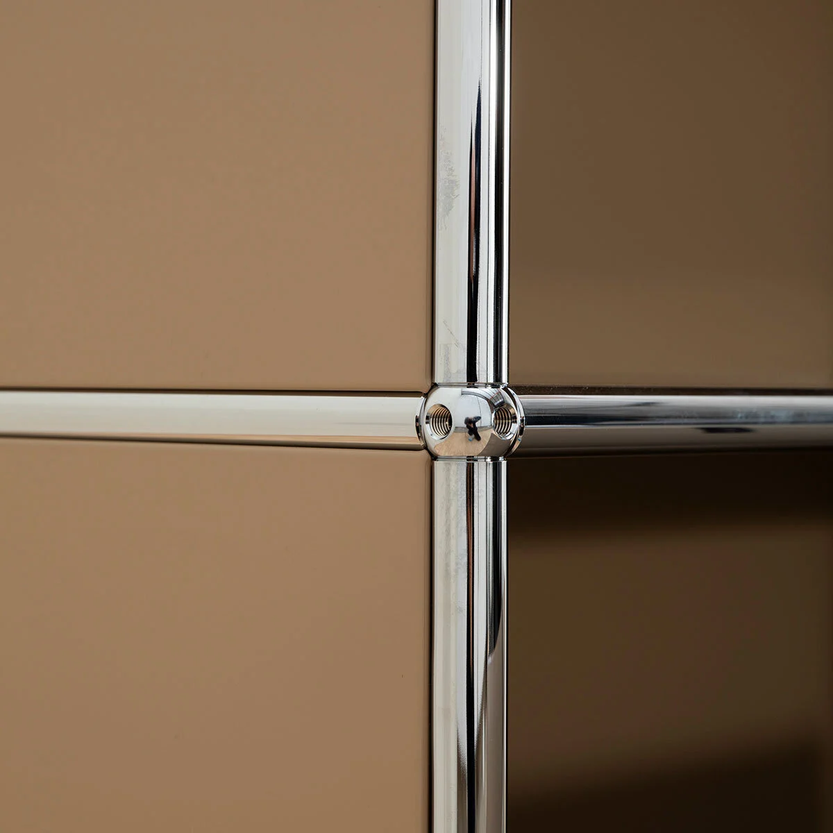 Chrome ball joint at the crossing of four frame tubes, against beige panels